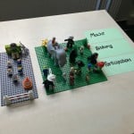 Menschen und Tiere als Legofiguren, daneben Karten mit Aufschrift "Macht", "Bildung" und "Partizipation"