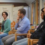 4 Personen sitzen auf Stühlen in einem Seminarraum nebeneinander und sprechen miteinander