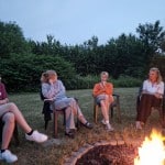 4 junge Menschen sitzen auf Stühlen an einem Lagerfeuer und unterhalten sich