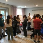 Junge Menschen stehen in einem Seminarraum eng nebeneinander in mehreren Kleingruppen und diskutieren